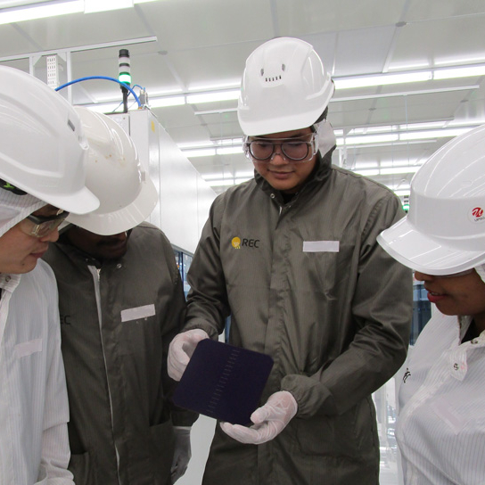 Four REC employees inspect a high-efficiency HJT solar cell at REC’s state-of-the-art solar manufacturing facility in Singapore