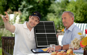 An REC Certified Solar Professional installer points to the sun and shows an REC Alpha solar panel to a customer interested in home solar